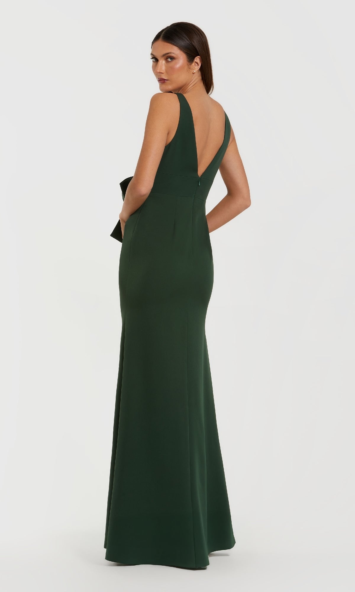 A woman stands against a plain white background, wearing the Bow-Front Green Formal Dress: Mac Duggal 50087—an emerald long gown with a deep V-back that exudes timeless elegance and sophistication.